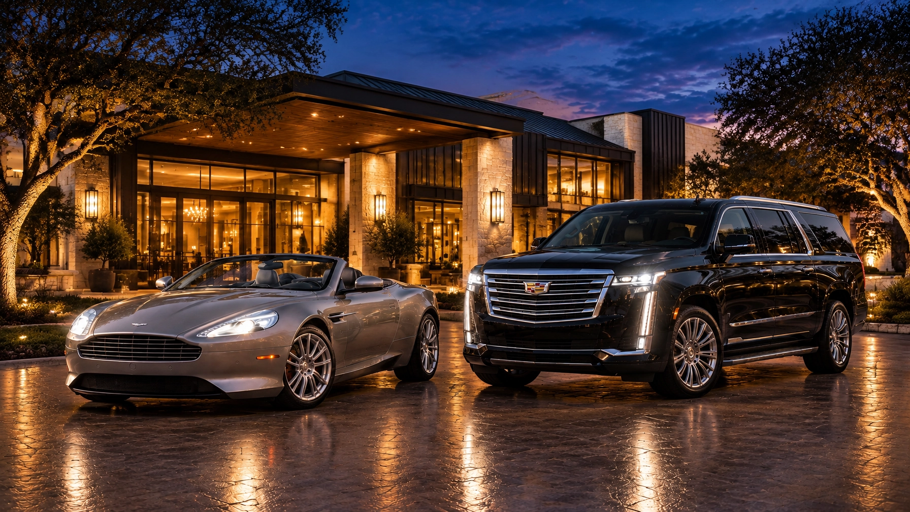 Silver-grey Aston Martin DB9 Volante and black Cadillac Escalade outside a modern Hill Country hotel at dusk